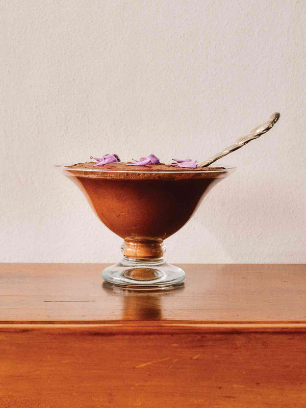 Chocolate cloud mousse in a glass coupe topped with purple flower petals and a silver spoon