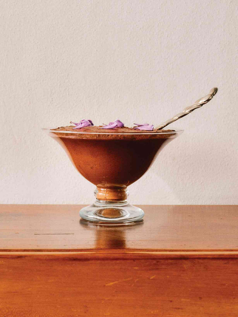 Chocolate cloud mousse in a glass coupe topped with purple flower petals and a silver spoon