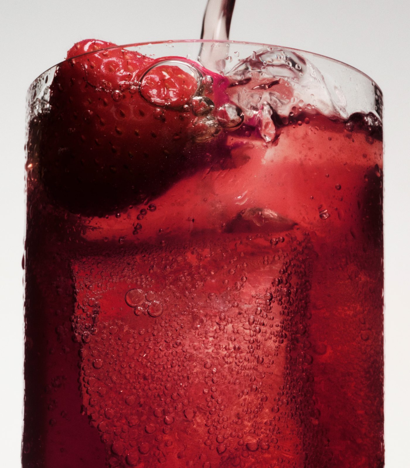 Close-up of a berry-red Ghia spritz being poured over ice with a strawberry