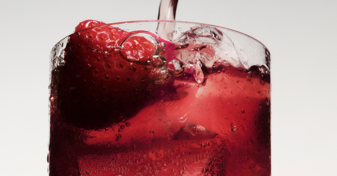 Close-up of a berry-red Ghia spritz being poured over ice with a strawberry