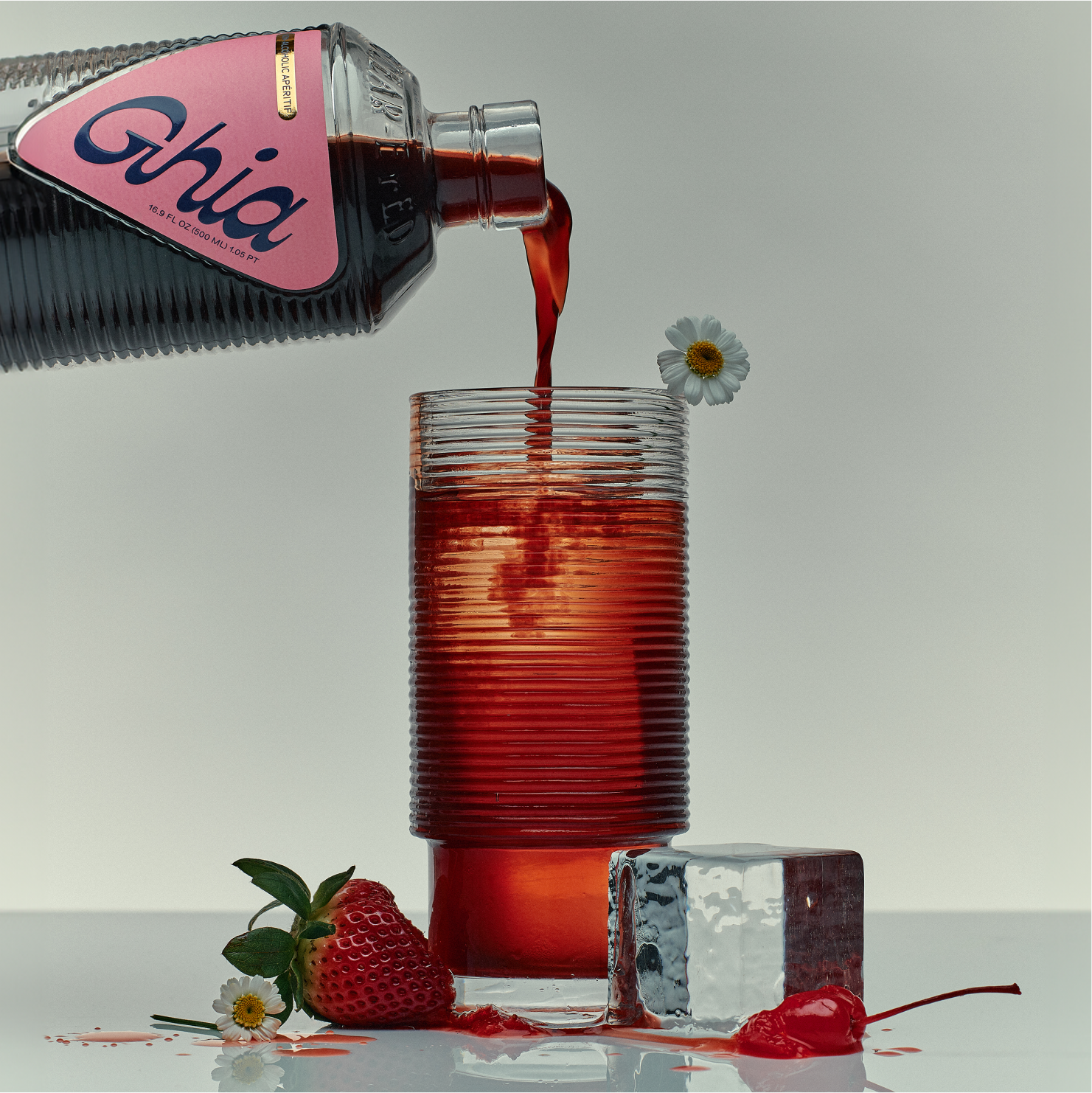 Ghia Berry apéritif poured from the bottle into a ribbed glass with strawberries and daisies