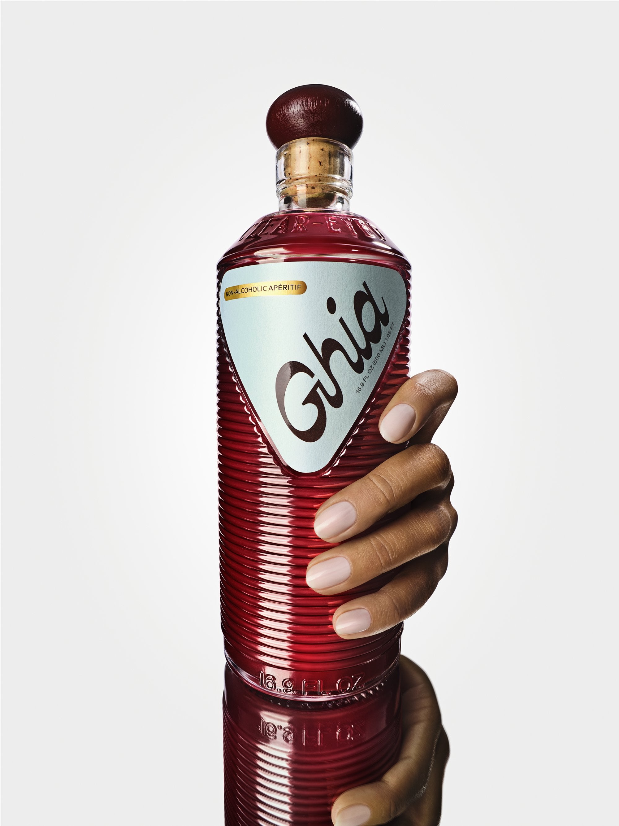 Hand gripping a ribbed red bottle of Ghia non-alcoholic aperitif