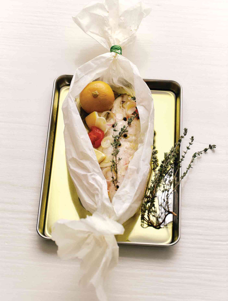 Fish baked en papillote with lemon, tomatoes, and thyme on a gold tray
