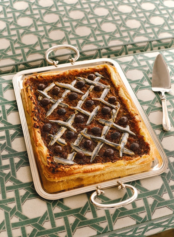 Pissaladière topped with anchovies and olives on a silver tray with a serving spatula
