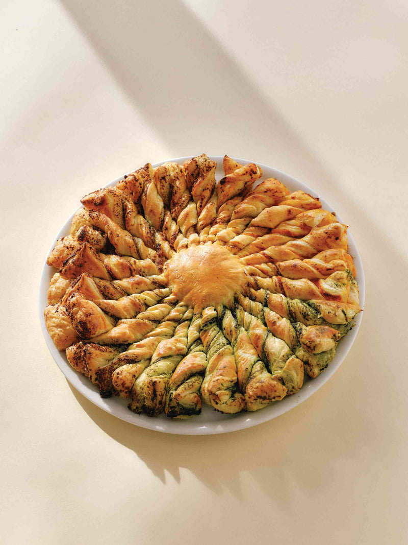 Tarte soleil with twisted pesto pastry spirals on a white plate