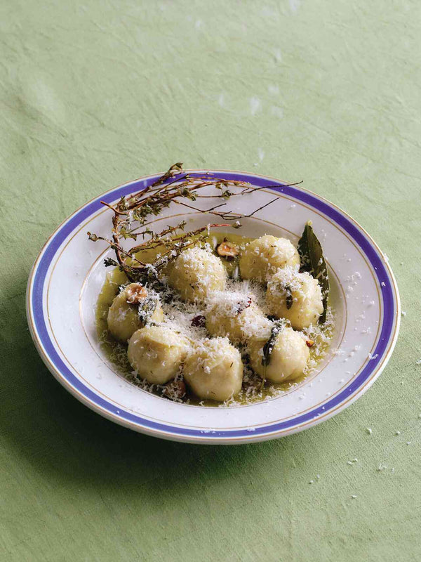 Ricotta gnudi with sage butter, grated cheese, and thyme on a blue-rimmed plate