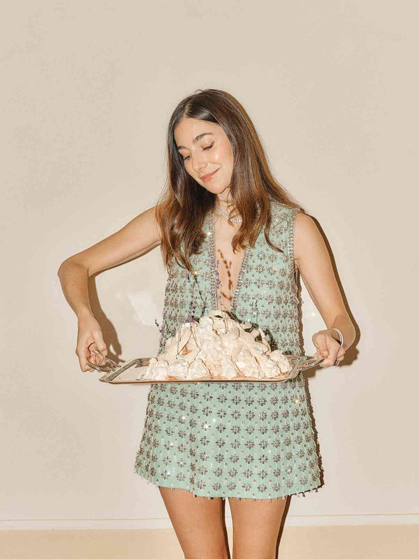 Smiling woman in a sequined mint dress holding a silver tray piled with meringue
