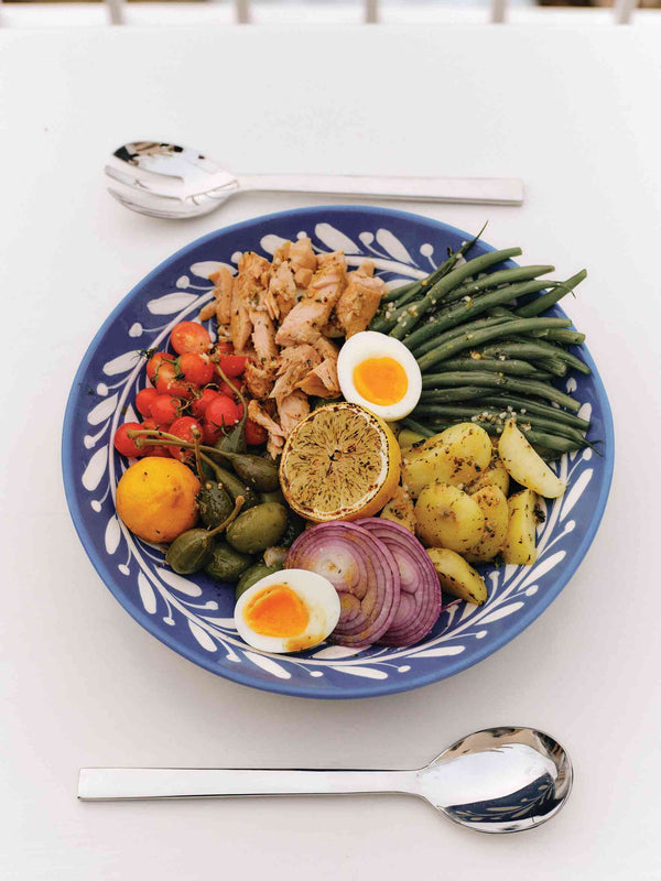 Salade niçoise with tuna, green beans, eggs, olives, and tomatoes on a blue patterned plate