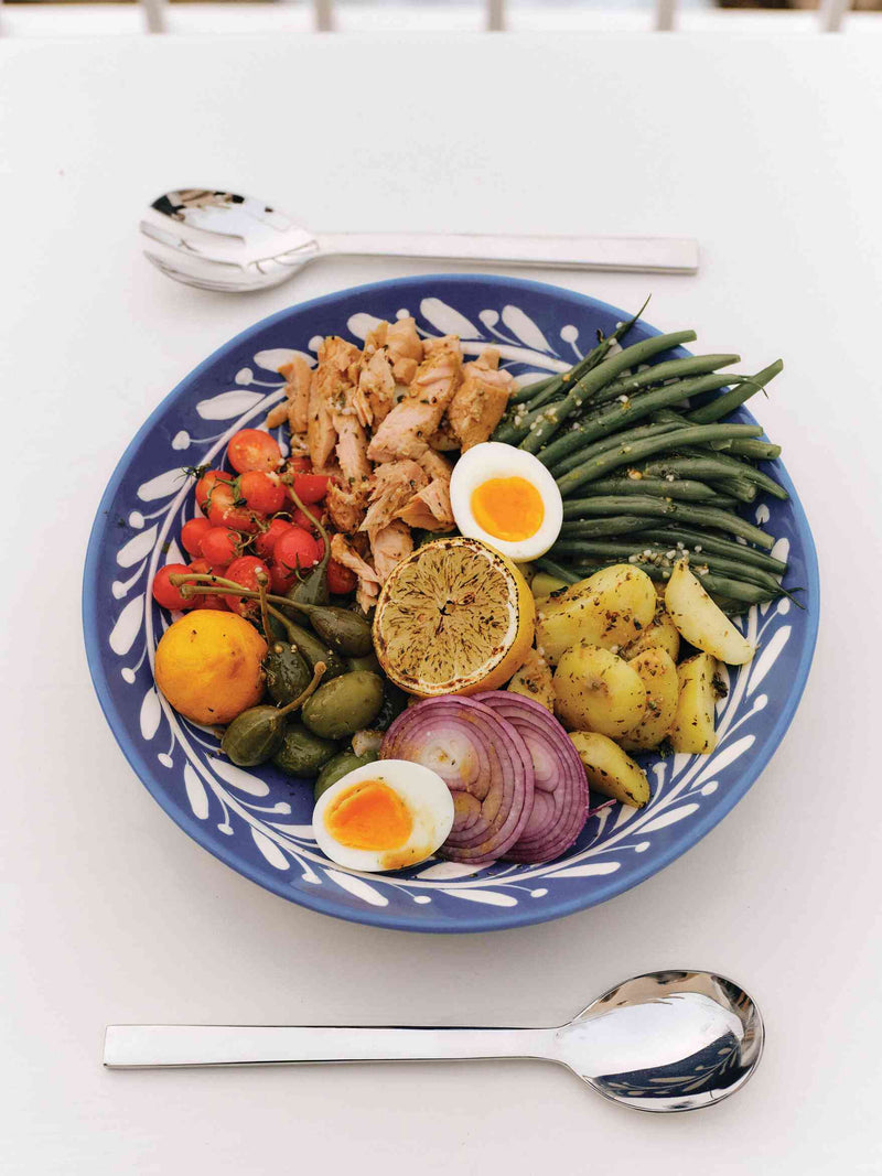 Salade niçoise with tuna, green beans, eggs, olives, and tomatoes on a blue patterned plate